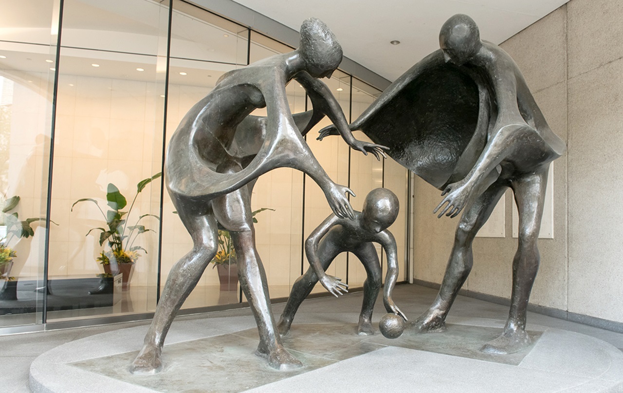A photograph of a bronze sculpture of three figures, a man, woman, and child, all playing with a ball depicted in an abstract style.