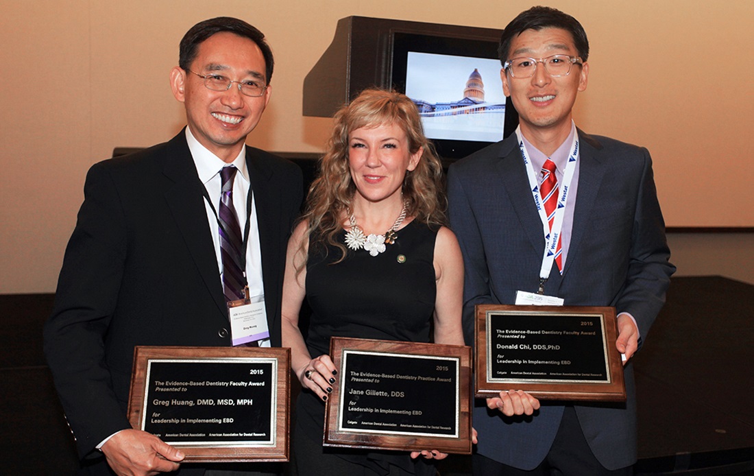 A photograph of two men and a woman. They smile at the camera while presenting awards that they have each received.