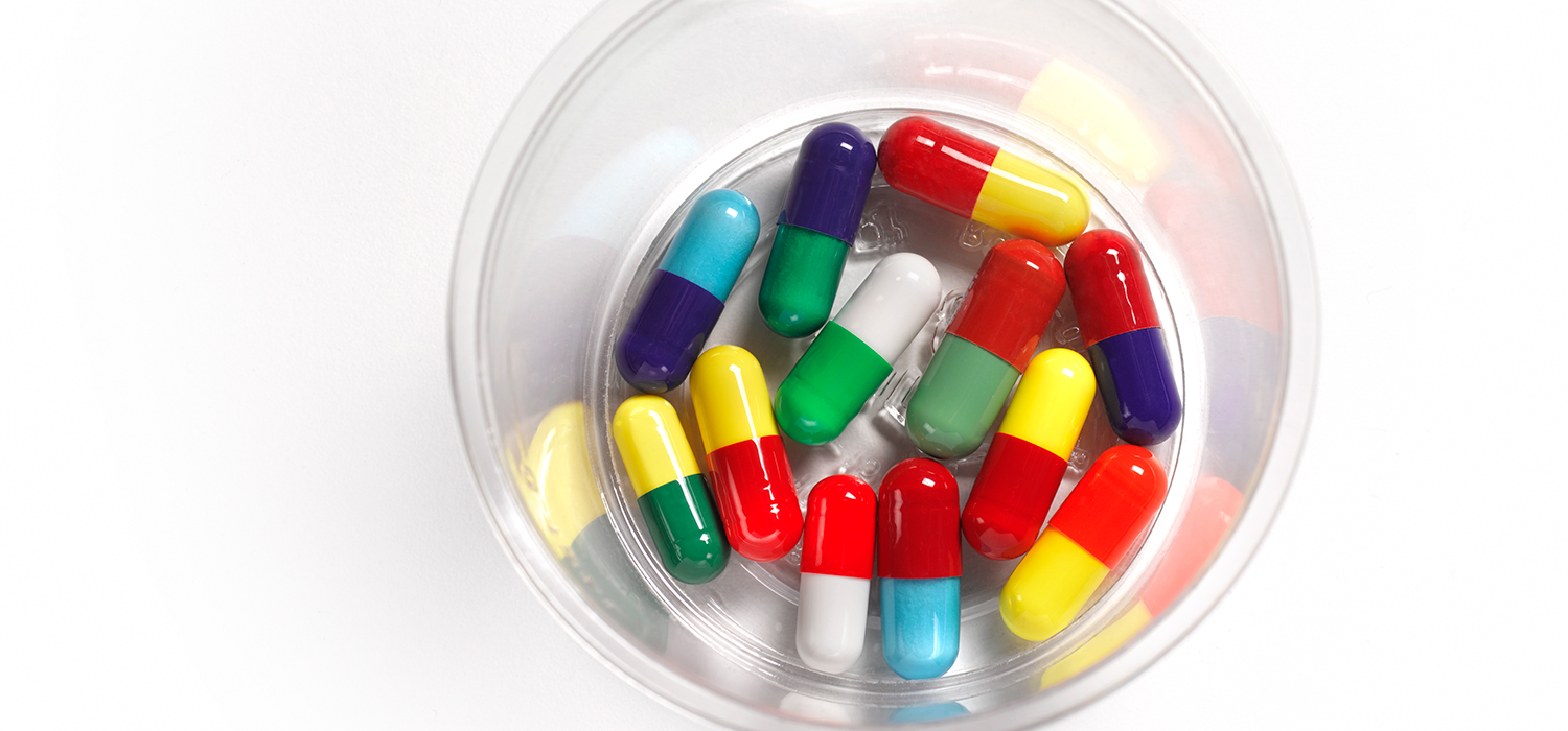 A photograph of twelve medicine capsules of various colors in a clear plastic disposable cup.