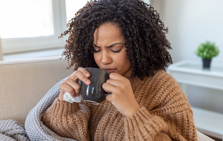 Woman not feeling well drinking tea holding Kleenex