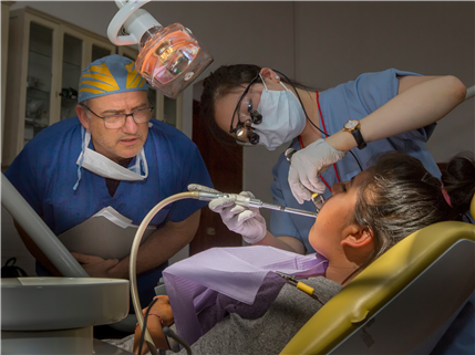 two dentists looking over chair to exam young girl