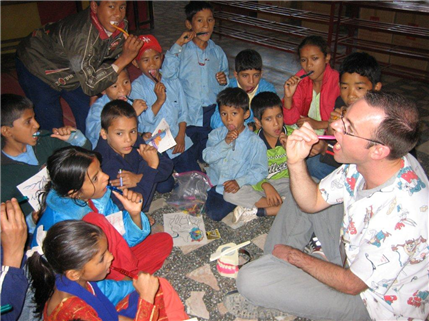 volunteer sitting on floor with children brushing teeth