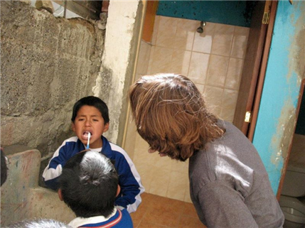 Young child brishing teeth as volunteer looks on