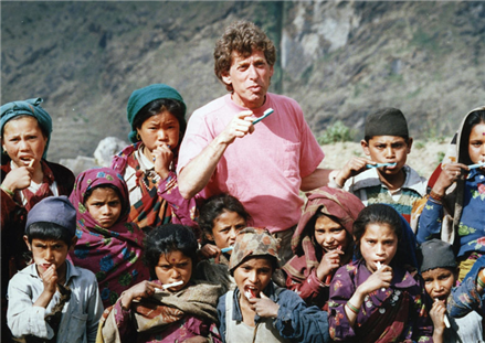 Dentist in Nepal with toothbrush surrounded by kids