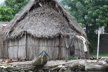 Photo of a grass hut with a canoe in front