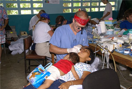 Photo of dental volunteer providing care to mom while a baby lies on her stomach