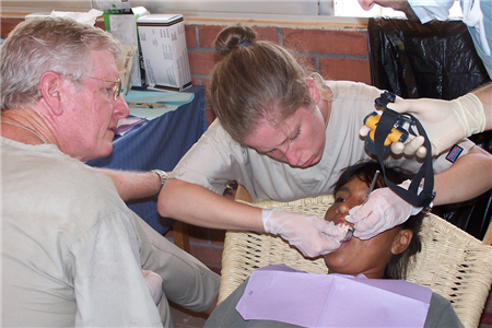 Photo of volunteers providing care in a clinic while a person holds a head lamp to provide light