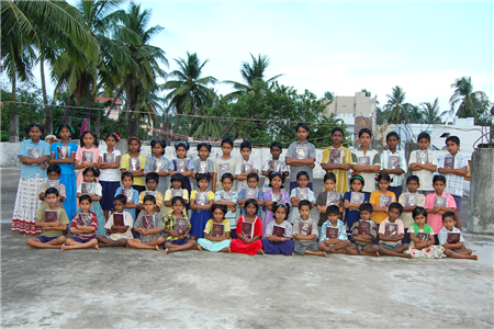 Photo of about 45 school kids of varying ages with books and palm trees in the background