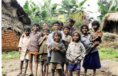 Photo of twelve smiling children with huts and palm trees in the background