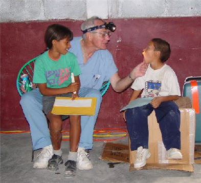 Photo of dental volunteer checking a child's mouth while another child observes