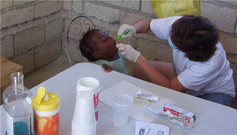 Photo of dental volunteer checking a small child's mouth by table