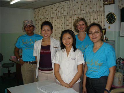 A dental team of five people posing against a flowered curtain
