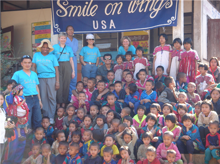 A large group photo of kids and adults near a Smiles on wings banner