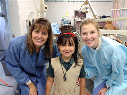 Photo of a smiling child with missing front teeth and two dental volunteers