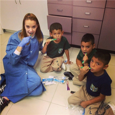Photo of a dental volunteer sitting on the floor with kids, teaching them how to brush their teeth