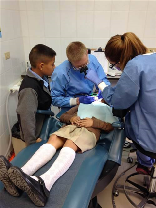 A dental team treats a child while a small boy looks on