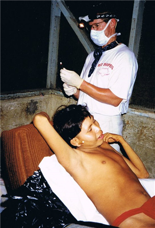 Photo of a dental volunteer providing care to a youth wearing a red loincloth