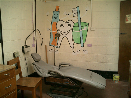Photo of a cinderblock wall with a dental themed mural, and a dental chair