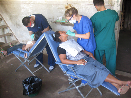 Photo of dental care providers treating people on back-to-back portable dental chairs