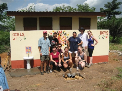 Photo of nine people posing in front of a mural with hand prints