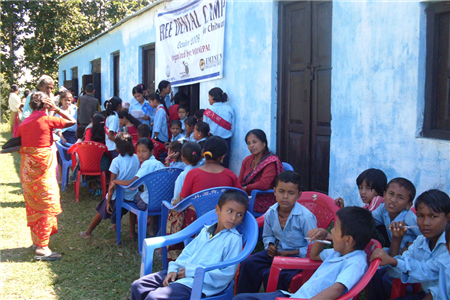Photo of kids and adults in plastic chairs outside of a blue building