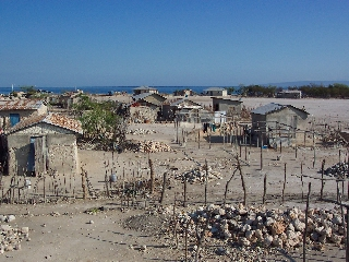 Photo of small shanty buildings on packed earth under a blue sky