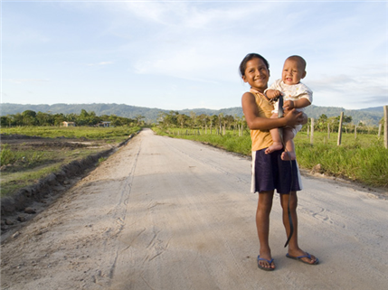 Photo of child holding a baby, standing on a dirt road